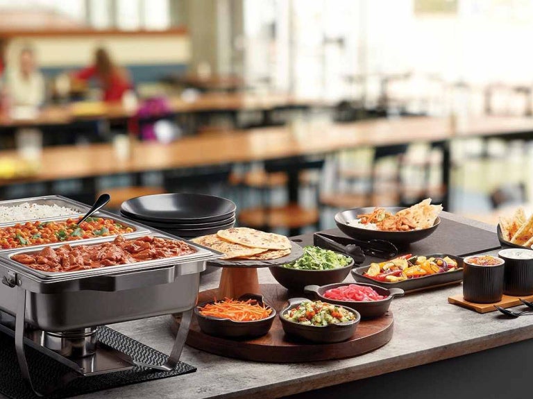 Una food station con diferentes platos, guarniciones y salsas donde los comensales pueden servir su comida.