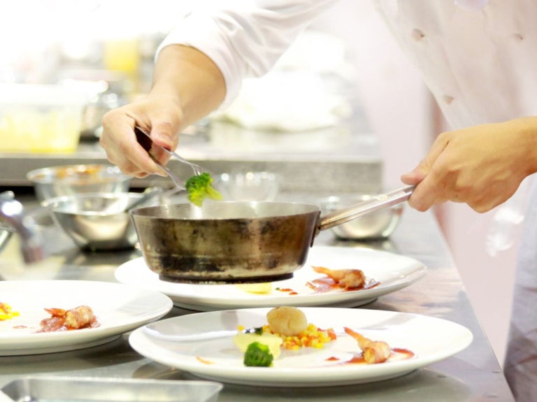 Chef emplatando platos cuidadosamente en cocina profesional, enfoque en calidad tipo Bib Gourmand