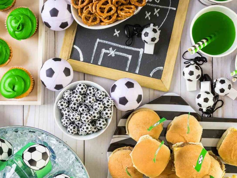 Mesa con snacks y bebidas decoradas con temática de fútbol para servicios de comida en eventos