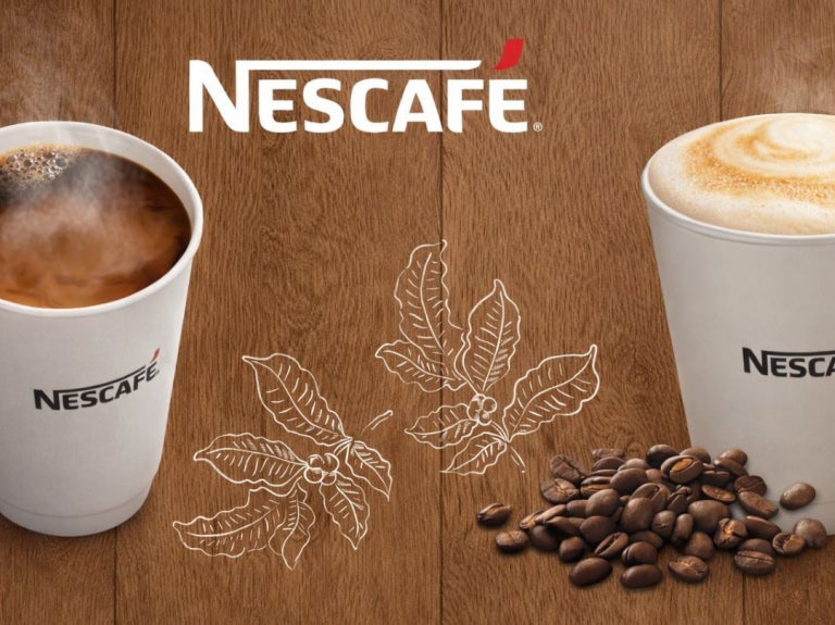 Dos vasos de NESCAFÉ con café americano y cappuccino de calidad, al pie, granos tostados