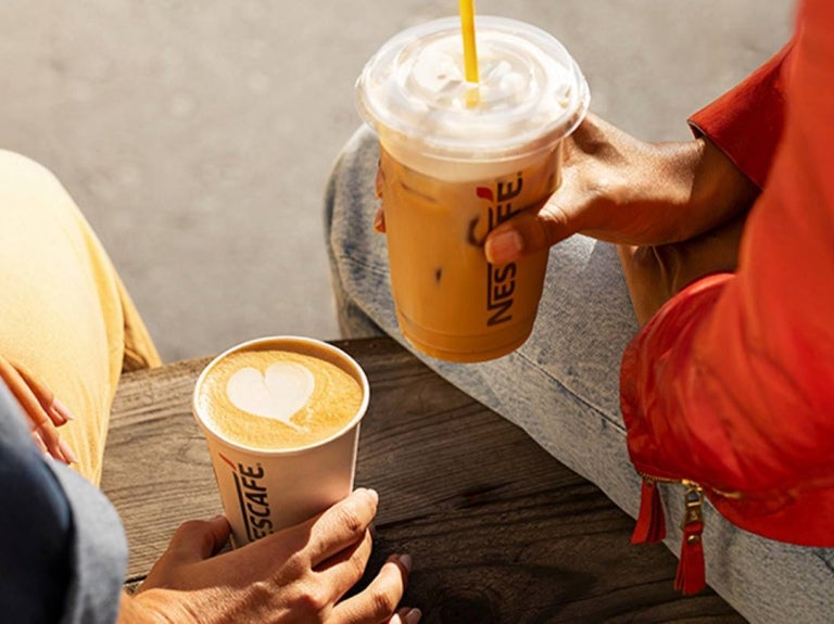 Dos personas sostienen una bebida caliente y una fría servidas en vasos de NESCAFÉ®