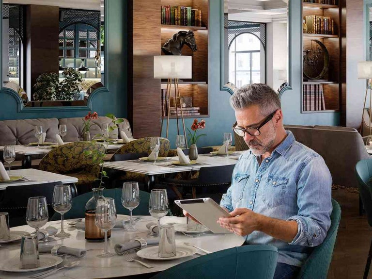 Persona revisa información en tablet dentro de un restaurante para hacer un comparativo de precios.