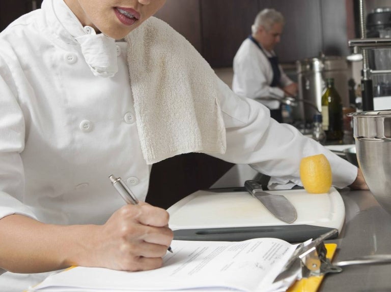 Chef revisa documentos en cocina profesional para identificar cuellos de botella en la operación.
