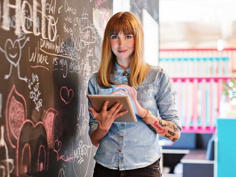 Mujer usa una tablet junto a un tablero con ideas en un espacio creativo.