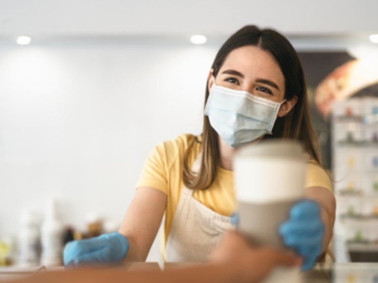 Trabajadora con mascarilla entrega una bebida como parte del servicio de alimentos en hospitales.
