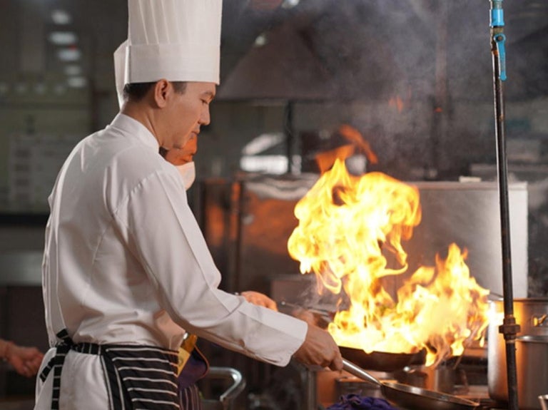 Chef cocinando con sartén en llamas en una cocina profesional, en plena acción culinaria