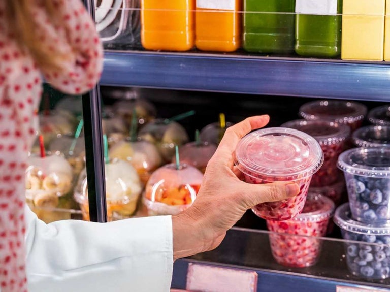 Persona revisa envase con frutas en refrigerador, ejemplo de etiquetado de alimentos.