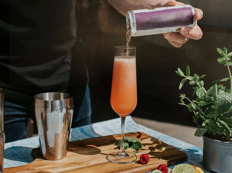Persona sirviendo una bebida artesanal en copa alargada, decorada con menta, cítricos y frutos rojos