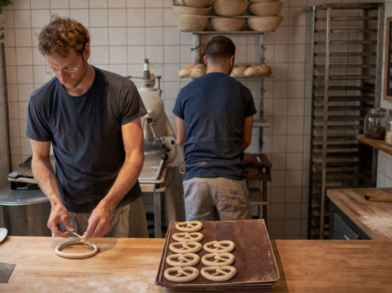 Panaderos elaborando masa en cocina compacta con bandejas listas para hornear en espacio reducido