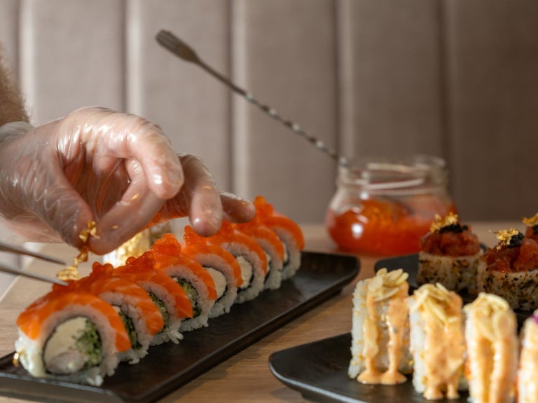 Chef decora sushi con oro comestible para elevar la presentación en cocina profesional.