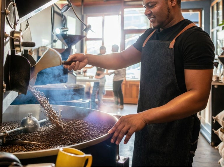 Barista manipulando máquina tostadora mientras vierte granos de café durante proceso de tueste