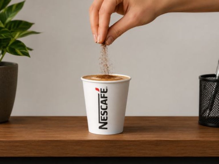 Mano espolvoreando ingrediente sobre taza de café en superficie de madera