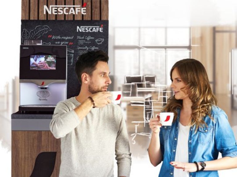 Hombre y mujer sosteniendo tazas frente a máquina de café en una cafetería de oficina