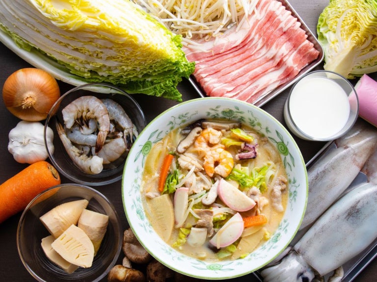 Vegetales, mariscos y carne frescos dispuestos alrededor de un plato con champon de Nagasaki