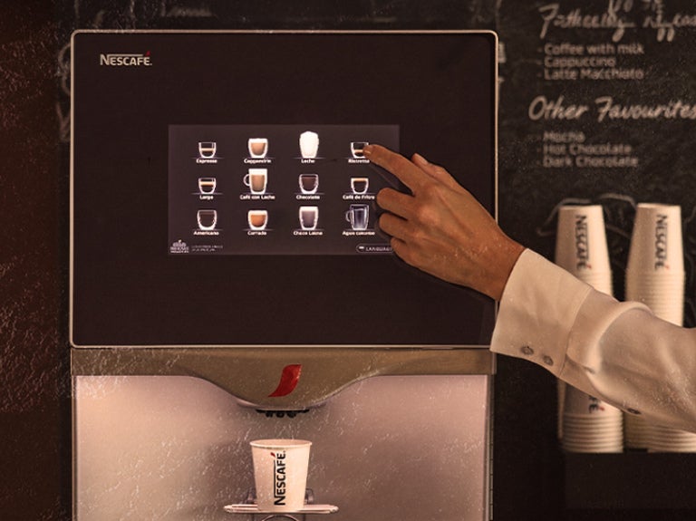 Mano seleccionando bebida en pantalla táctil de máquina de café con vaso debajo