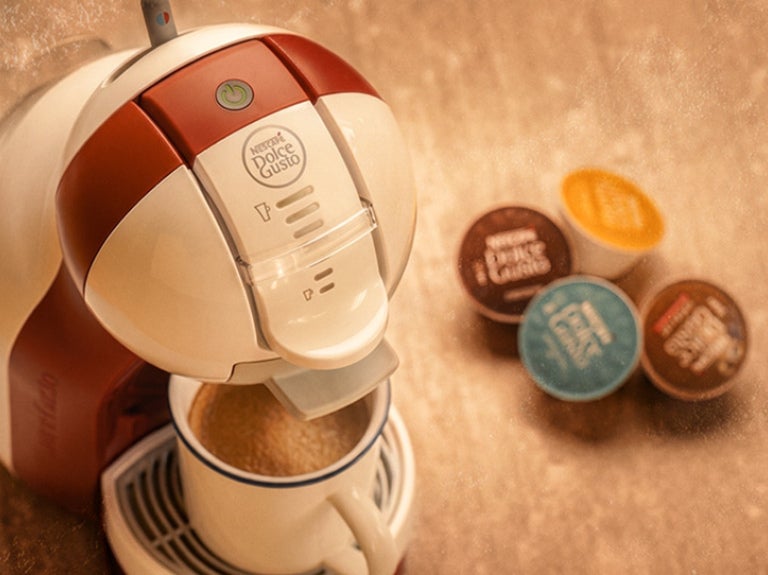 Máquina NESCAFÉ® Dolce Gusto® preparando bebida con cápsulas de colores al lado