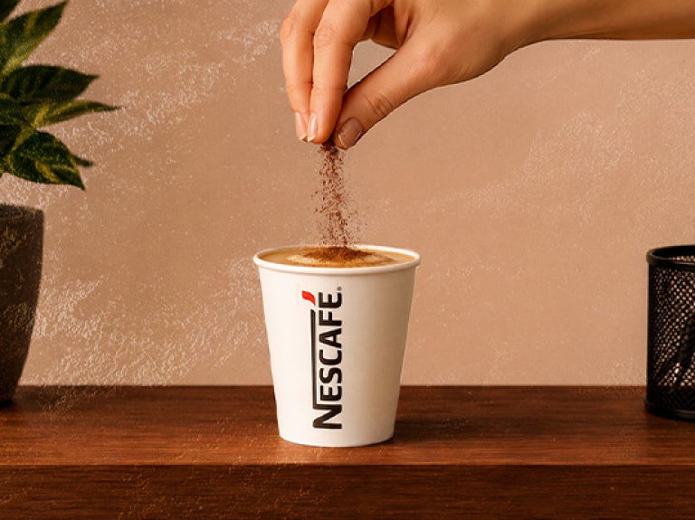Mano espolvoreando ingrediente sobre taza de café en superficie de madera