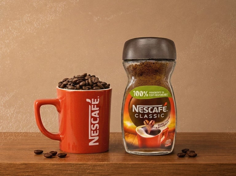 Frasco de café soluble junto a taza roja de NESCAFÉ® con granos de café