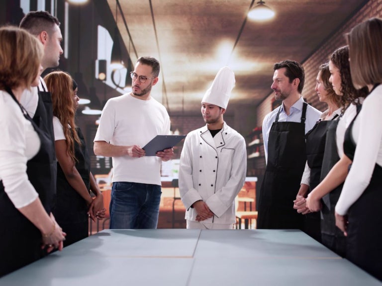 Grupo de personas reunidas en cocina profesional mientras una persona explica con una tablet