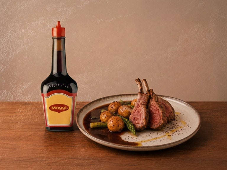 Botella de sazonador MAGGI® junto a un plato con carne y papas con salsa servidos en la mesa