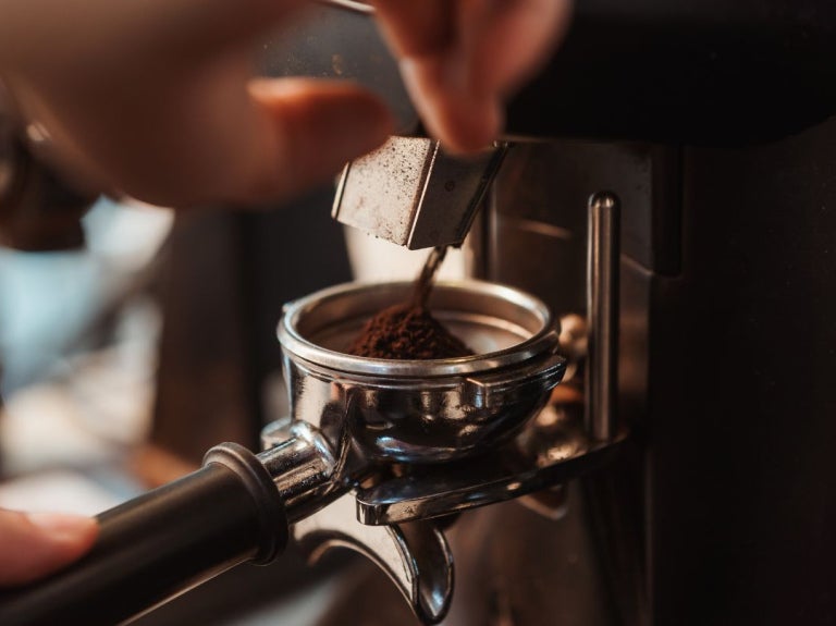Persona coloca café molido en el portafiltro de una máquina de espresso