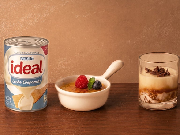 Lata de Leche Evaporada NESTLÉ® IDEAL® con postres cremosos sobre una mesa