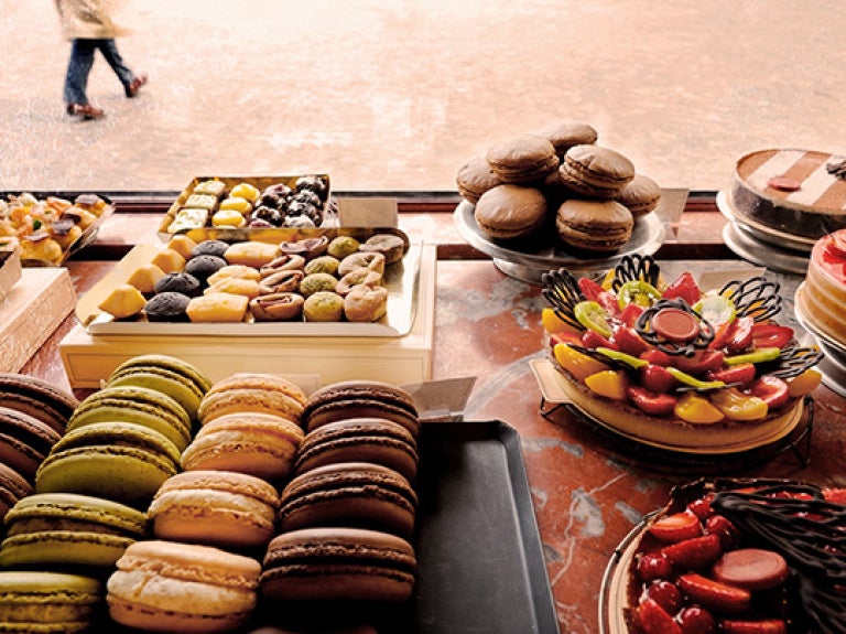 Exhibición de postres variados en una vitrina como macarons, frutas y pasteles sobre mostrador