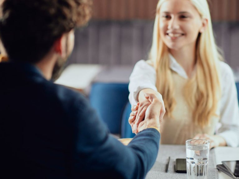 Dos personas se dan la mano sobre una mesa con vaso de agua y teléfono