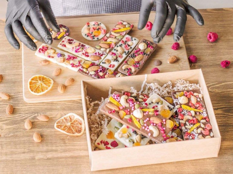 Repostera coloca barras de chocolate artesanal decoradas con frutos secos liofilizados en una caja.