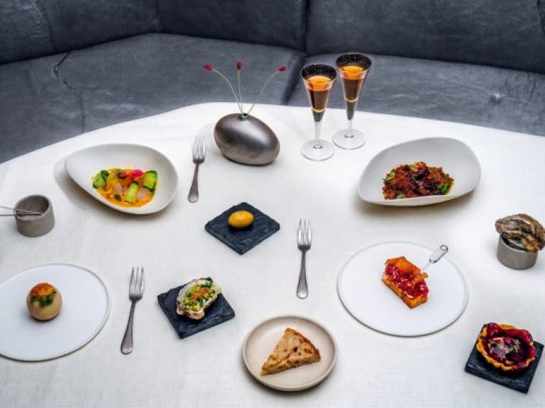 Varios platillos gourmet servidos sobre una mesa con mantel blanco y dos copas de vino fino.