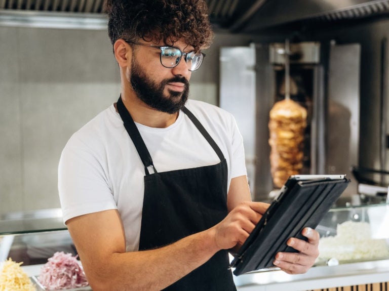 El propietario de un restaurante registra pedidos en una tableta digital junto al mostrador.