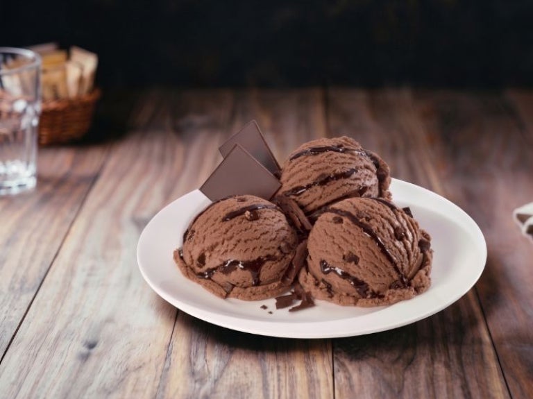 Tres bolas de helado de chocolate con jarabe de café y trozos crujientes sobre un plato blanco.