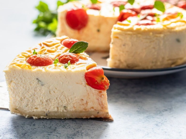 Rebanada de pastel salado de queso decorada con tomates cherry sobre una espátula de servir.