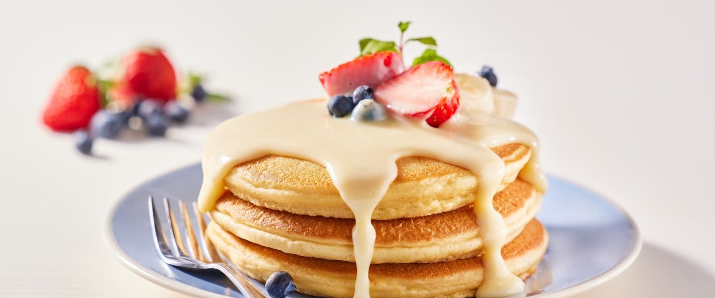 Panqueques con crema, cubiertos con fresas y arándanos, hecho posible por un proveedor de lácteos al por mayor