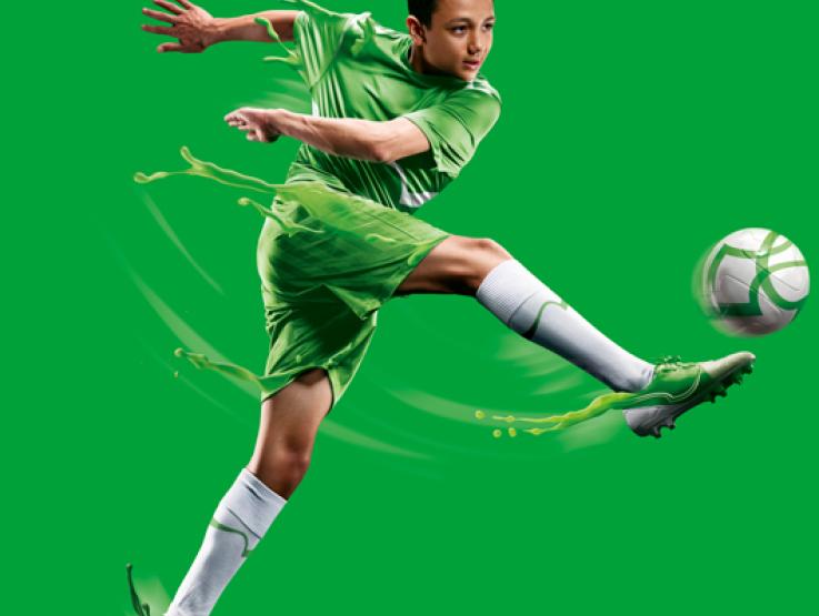 Joven con uniforme verde pateando un balón de fútbol
