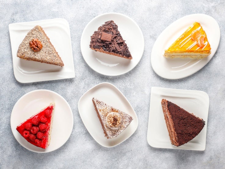 Seis rebanadas surtidas de pastel en platos blancos, hechos con productos de un proveedor de lácteos al por mayor.