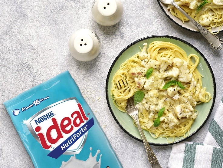 Un plato de pasta cremosa con hierbas se encuentra junto a un paquete de leche IDEAL® NutriForte professional.