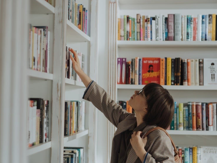 Mujer con gafas tomando un libro de la biblioteca