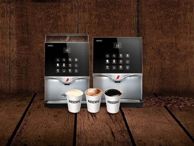 Dos máquinas NESCAFÉ® para negocios de café en grano y soluble, al frente tres vasos desechables de leche, cappuccino y café