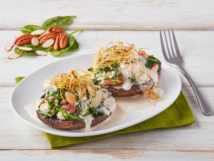 Sobre una mesa de madera un plato con portobellos rellenos en salsa de nuez elaborada con CARNATION® y al lado un tenedor