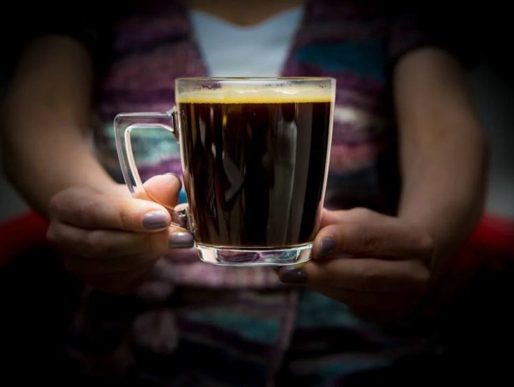 Taza de café en vidrio sostenida por una mujer, preparación elaborada con NESCAFÉ®