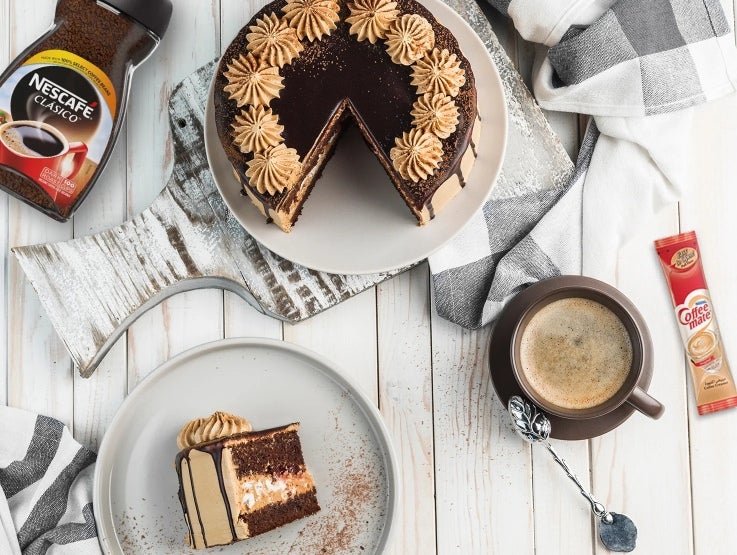 Una rebanada de pastel de chocolate y alrededor un frasco de café y crema para café de un proveedor al por mayor.