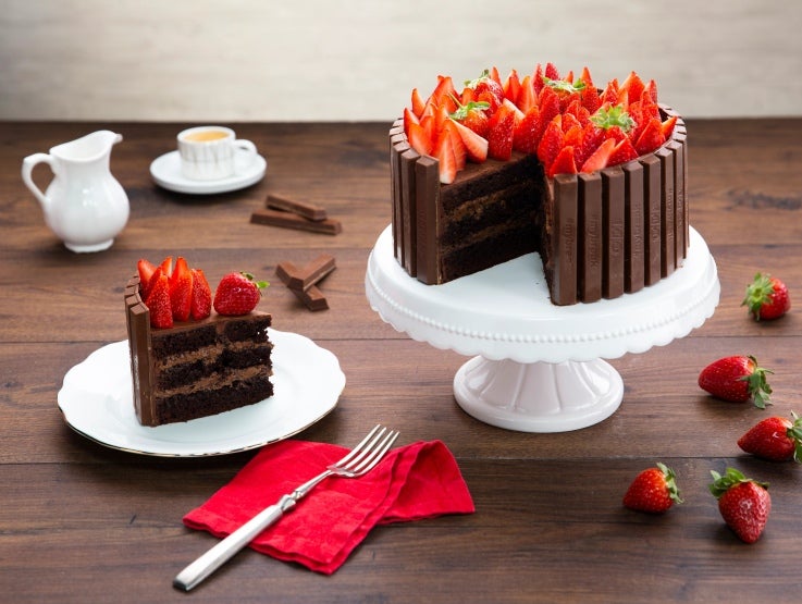 Pastel de chocolate decorado con fingers KITKAT® Professional y fresas sobre una base blanca.