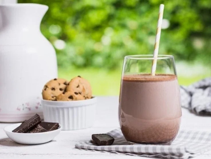 Sobre una mesa, un vaso de bebida de chocolate, tabletas de chocolate, galletas y una botella de leche