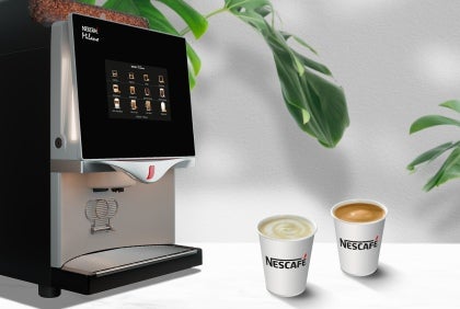 Máquina de café profesional NESCAFÉ® con dos tazas de café sobre una encimera blanca, ideal para negocios.