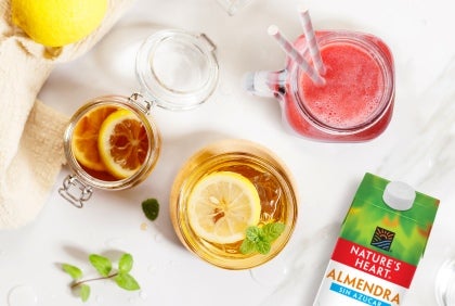 Vasos de vidrio con bebida rosa y té con limones y menta junto a una caja de Nature’s Heart Almendra sin Azúcar
