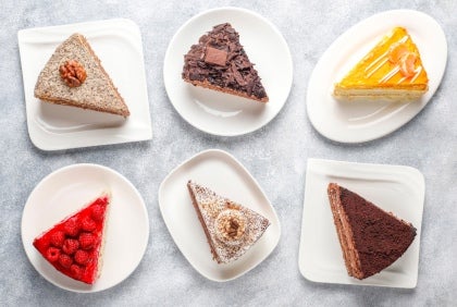 Seis rebanadas surtidas de pastel en platos blancos, hechos con productos de un proveedor de lácteos al por mayor.