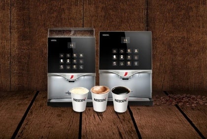 Dos máquinas de café profesionales para negocios NESCAFÉ® con tres tazas de café sobre una superficie de madera.