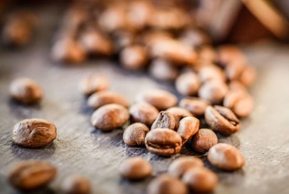 Granos de café tostados, uno de los insumos esenciales para las máquinas de café, esparcidos sobre una mesa.