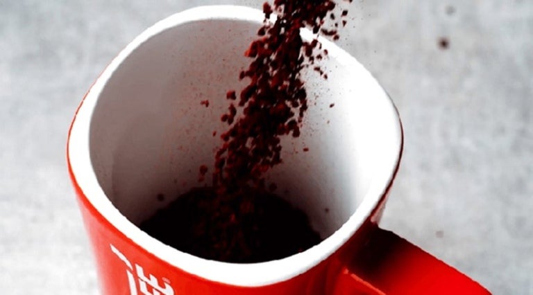 Café instantáneo granulado cayendo en una taza color rojo en su exterior y blanco en el interior de Nescafé